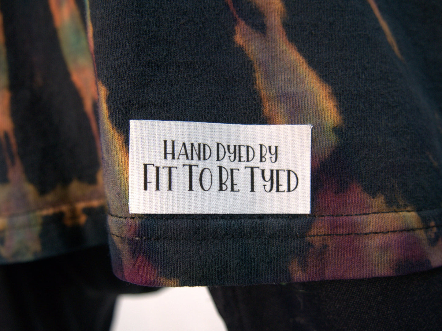 Ocular Reverse Tie Dye T Shirt using a Spiral Design in Green, Orange and Black, in size Large, showing label detail on front bottom left of shirt (Original White Label!)